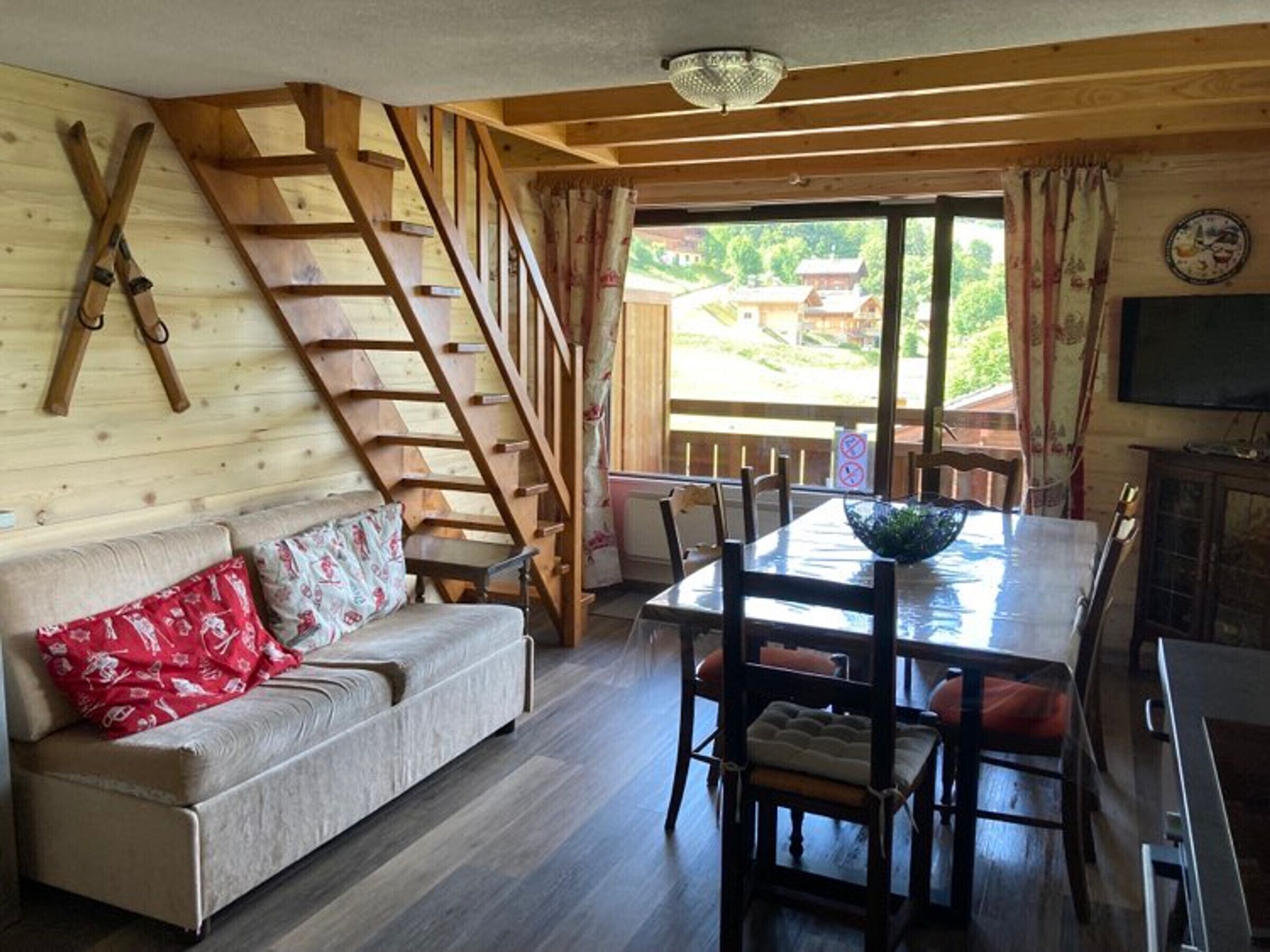 A wooden interior with a sofa, dining table, chairs, and a ladder.