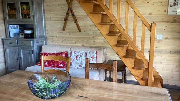 Una mesa de comedor de madera, una cesta tejida, una escalera de madera, un armario gris y un sofá con cojines estampados.