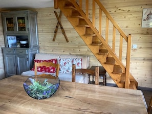 Ein Holztisch mit einem gewebten Korb, eine Holztreppe, ein grauer Schrank und eine Couch mit gemusterten Kissen.