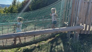 A rope bridge over a netted area with wooden posts, surrounded by greenery and trees. - Apartment - Am Roten Kreuz 11 | Züschen (Winterberg)