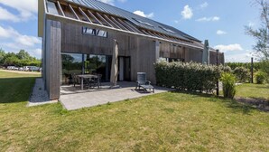 Un bâtiment moderne doté d’un toit en pente, de grandes fenêtres et d’un patio aménagé avec du mobilier d’extérieur.