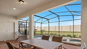 A covered patio with a pool, outdoor seating, and a view of the backyard. - Westside Charm | Games Room | Kids Bedrooms (Kissimmee)
