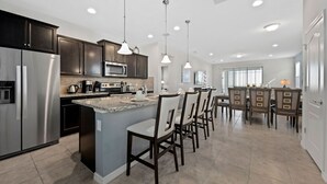 A modern kitchen with stainless steel appliances, dark wooden cabinets, and a central island with bar seating. - Westside Charm | Games Room | Kids Bedrooms (Kissimmee)