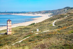 A coastal landscape with a prominent tower structure, a sandy beach, and a winding path leading up the hill.