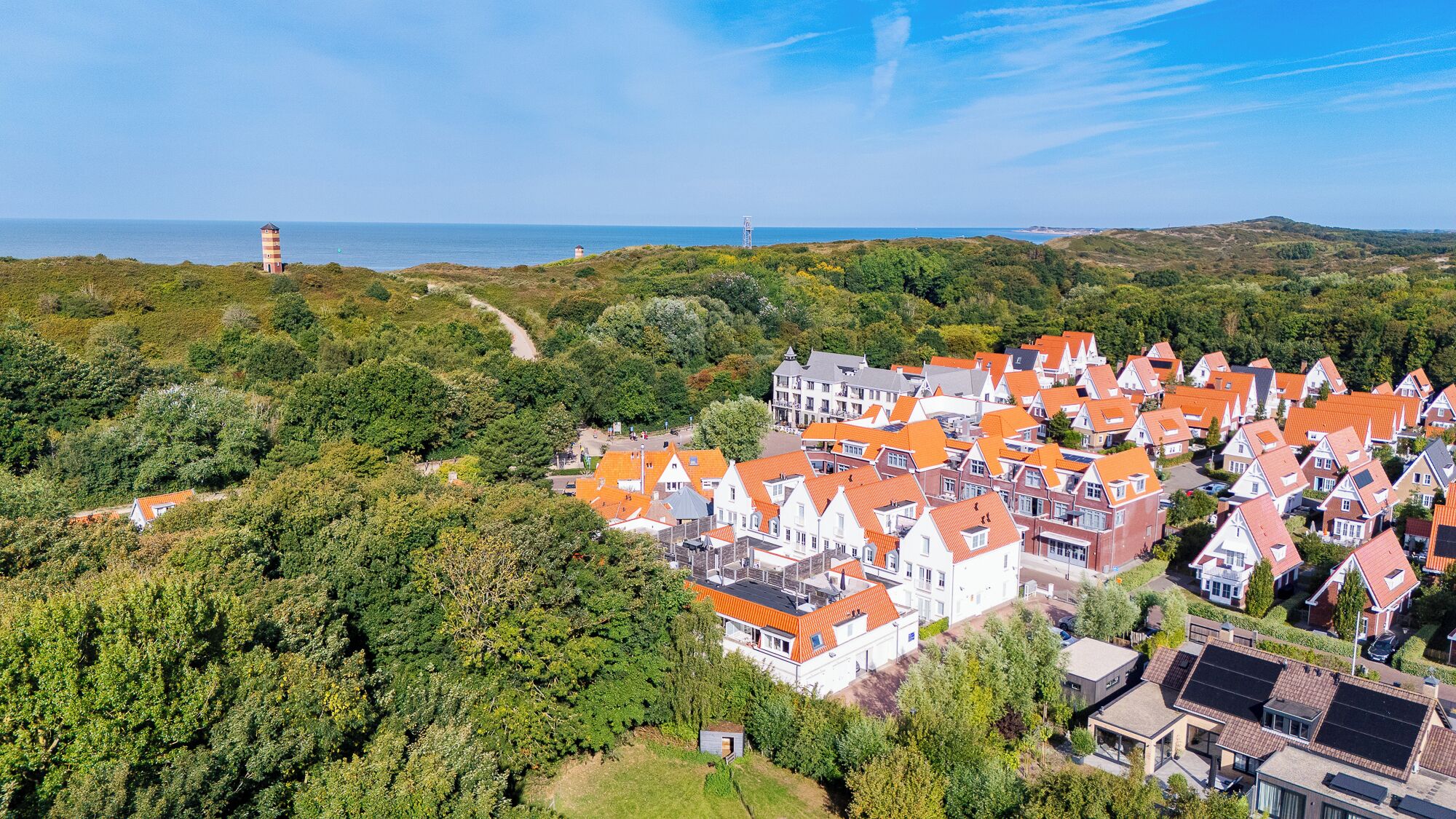 Eine Küstenstadt mit traditionellen Häusern mit roten Dächern, einem Leuchtturm und einer Mischung aus Wohn- und Geschäftsbauten.