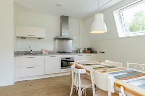 A modern kitchen with white cabinetry, a stainless steel range hood, and a wooden dining table with a colorful table runner.