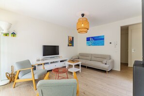 A living room with a television, sofa, chairs, a coffee table, and artwork on the walls.
