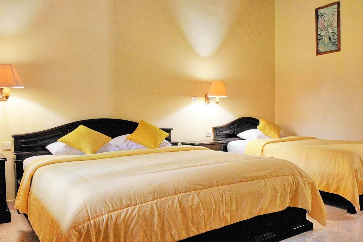 Hotellihuone, jossa on kaksi sänkyä, ja molemmissa on keltaiset lakanat ja tyynyt sekä kaksi yöpöytävalaisinta.