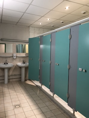 Baño público con dos lavamanos, cabinas color turquesa y un espejo sobre los lavamanos.