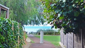 A pathway leading to a beach with a wooden structure on the left and a stone wall on the right.
