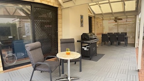 An outdoor patio with a grill, seating, and a glass door leading to a covered area.
