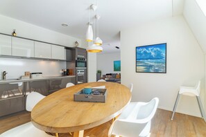 A modern kitchen with stainless steel appliances, a wooden dining table with chairs, and a view of the living area with a painting. - Apt - Kaapduinseweg 13 | Dishoek "13N Lu (Koudekerke)