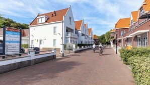 A street lined with traditional white buildings with red-tiled roofs, a paved walkway, and a signboard with text.