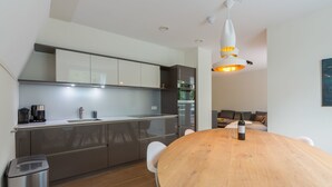 A modern kitchen with a wooden dining table, a coffee machine, and a wine bottle.
