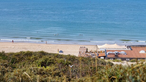 A beach with a sandy shore, a few people, and a building with a red roof in the foreground.