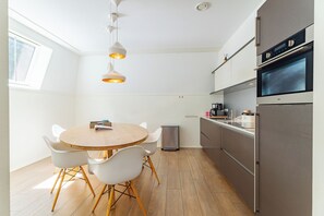 A modern kitchen with a round wooden table, white chairs, and stainless steel appliances.