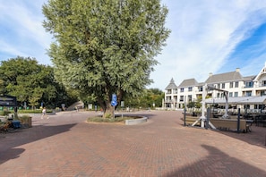 A paved square with a large tree, a blue parking sign, and a row of white buildings with gabled roofs.