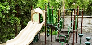 Ein Spielplatz mit Rutsche und Klettergerüsten, umgeben von viel Grün.