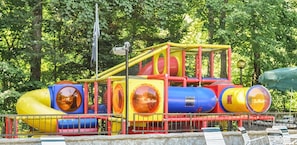 Ein farbenfrohes Spielgerät mit Rutschen und Tunneln, umgeben von Bäumen.