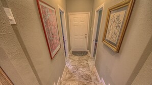 A hallway with a white door at the end, framed artwork on the walls, and a patterned rug on the floor.
