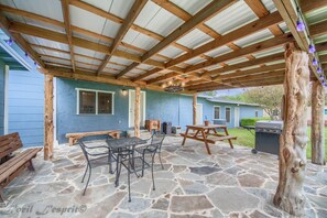 A covered patio with stone flooring, wooden beams, a metal table and chairs, a wooden bench, and a barbecue grill. - Zipp Away Ld 728 3 Bedroom Home by RedAwning (New Braunfels)