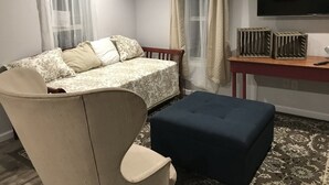 Un dormitori amb un llit, una cadira, una taula i una televisió.