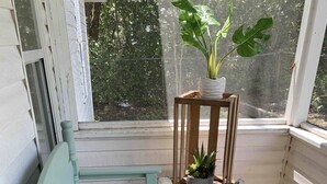 Una banca de fusta amb coixí, una taula petita amb una planta en test i una placa decorativa a la verada.