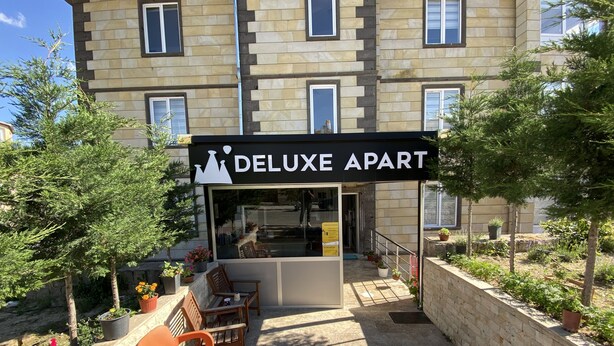 An outdoor seating area with a sign reading "DELUXE APART" in front of a building with multiple windows. - Kapadokya Deluxe Apart (Ürgüp)