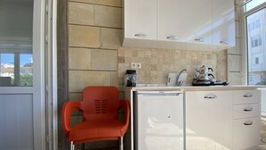 A compact kitchen with white cabinets, a small countertop, and a red plastic chair. - Kapadokya Deluxe Apart (Ürgüp)