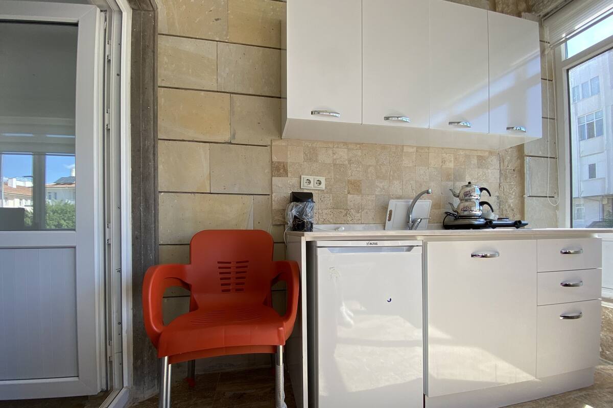 A compact kitchen with white cabinets, a small countertop, and a red plastic chair.
