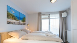 Ett hotellrum med en stor säng, två tavlor som hänger på väggen, ett fönster med gardiner och en taklampa.