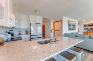 Una cocina moderna con una isla central, electrodomésticos integrados y una zona de estar con sofá y taburetes de bar.