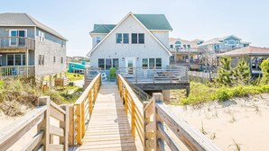 A beachfront property with a wooden boardwalk leading to a white building with a green roof.