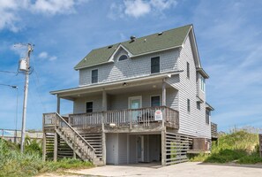 A two-story house with a front porch, a staircase leading to the entrance, and a visible utility pole with wires. - Wildest Dream - S Nags Head MP 17, Oceanfront, Direct Ocean Access, Air Hockey, Pets OK (South Nags Head)