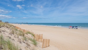 Una playa arenosa con un cerco de madera, un muelle y el océano.