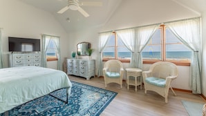 Un dormitorio con cama, televisor, cómoda, sillas de mimbre y vista al océano.