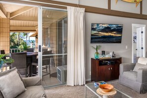 Een woonkamer met een glazen deur naar een balkon, een flatscreen televisie, een houten kast en een bank.