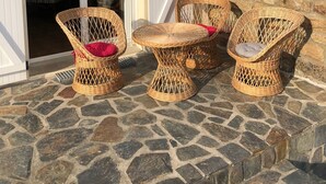 Un patio con suelo de piedra, mobiliario de mimbre y una puerta blanca que da a un espacio interior.