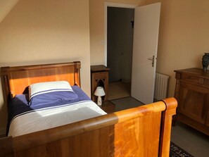 Een slaapkamer met een houten bed, een nachtkastje, een lamp en een dressoir.