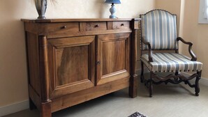 Un mueble de madera con cajones, una lámpara y una silla a rayas frente a una pared con un cuadro.