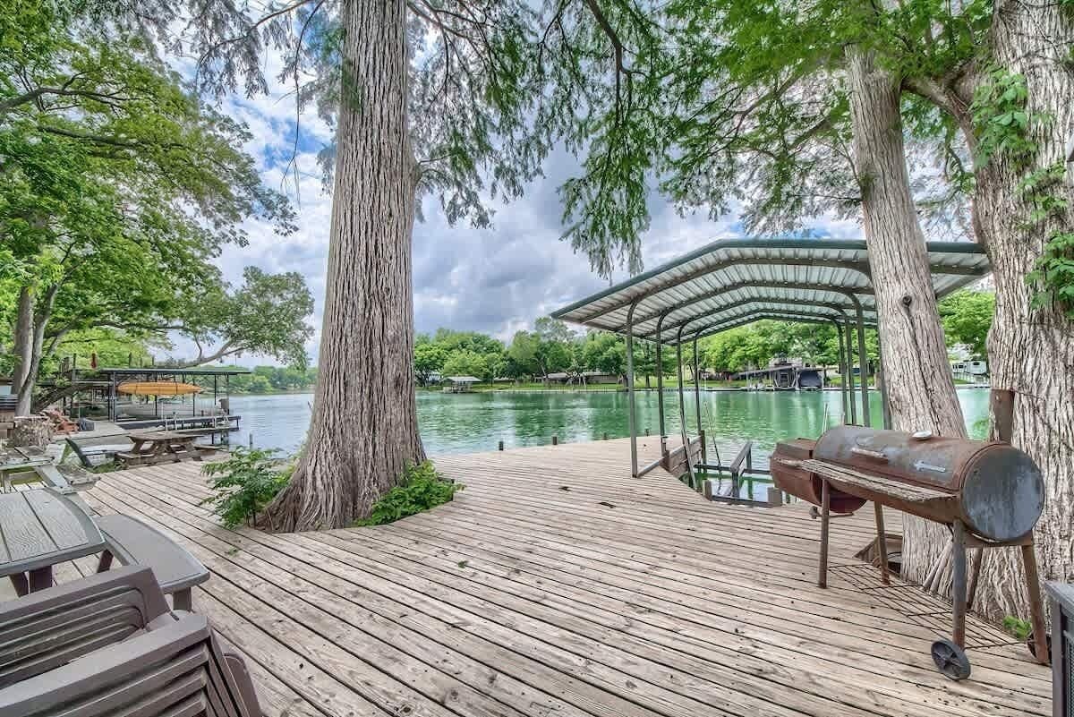 A wooden deck with a grill, a covered seating area, and a view of a lake.