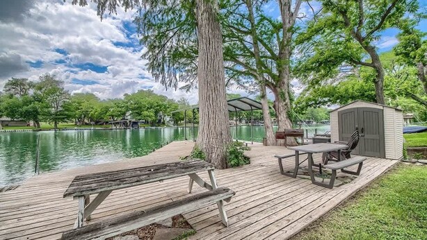 Une terrasse en bois avec des tables de pique-nique et un abri de jardin, le tout situé au bord d’un lac.
