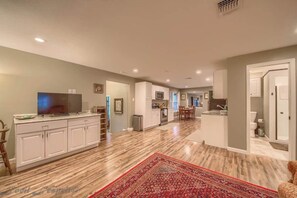 A spacious living area with a large TV, wooden flooring, and a red patterned rug.
