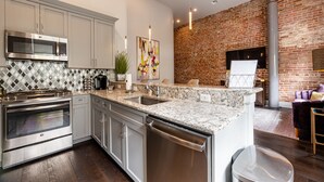 A modern kitchen with stainless steel appliances, a marble countertop, and a brick wall. - DOWNTOWN 2BR Walk to Superdome,Parade French Quarter (New Orleans)