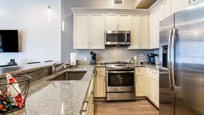 Una cocina moderna con gabinetes blancos, electrodomésticos de acero inoxidable, encimera de granito y microondas integrado.
