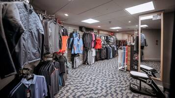 A clothing store with racks of jackets and shirts, a patterned floor, and a mirror on the right.