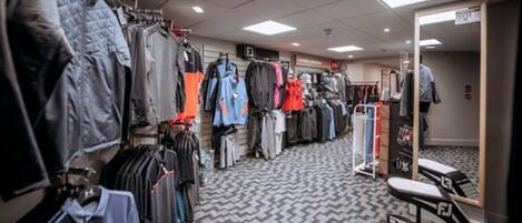 A clothing store with racks of jackets and shirts, a patterned floor, and a mirror on the right.