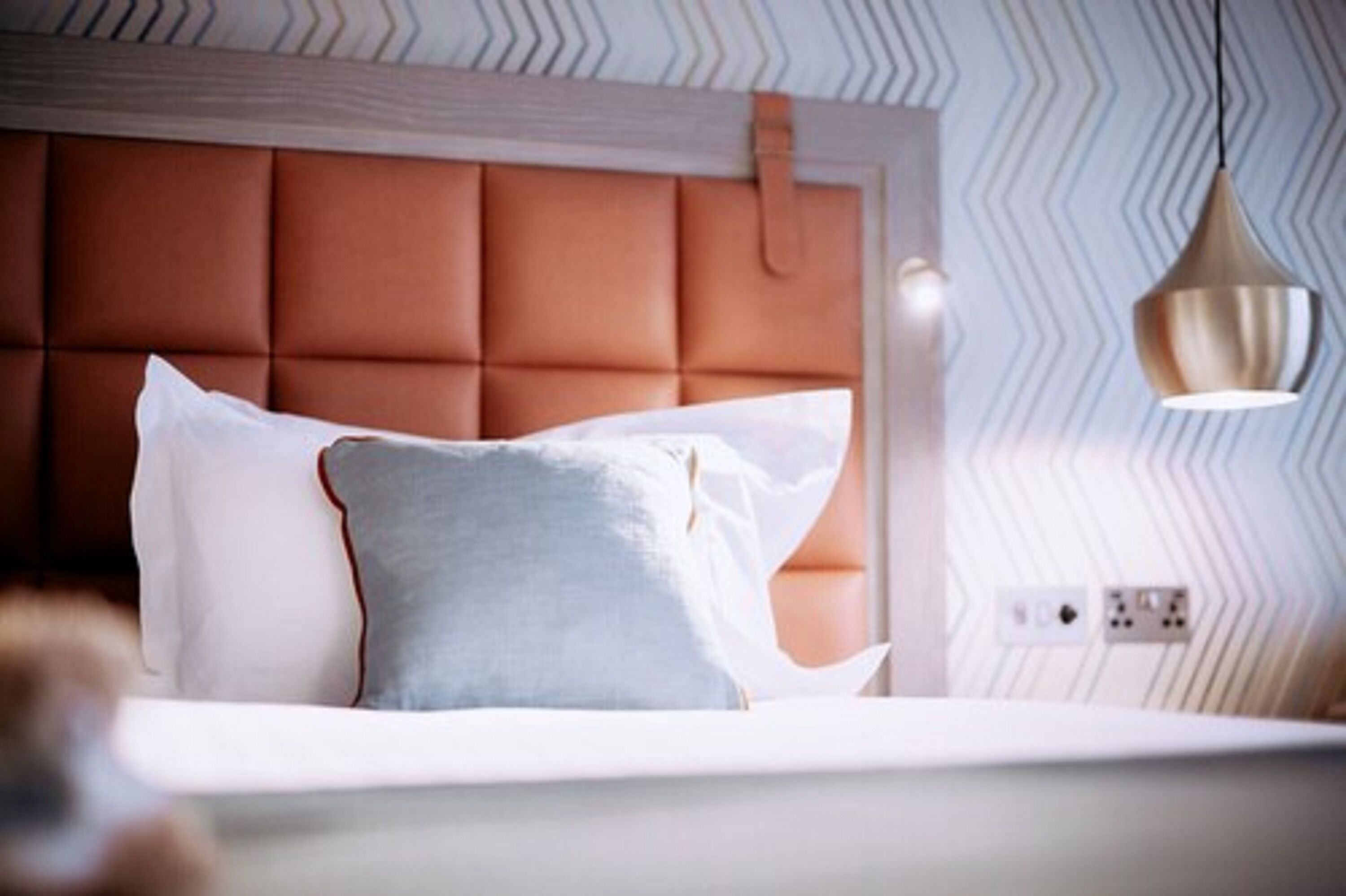 Un dormitorio con cabecera tapizada, cama con ropa de cama blanca y azul, e iluminación colgante.