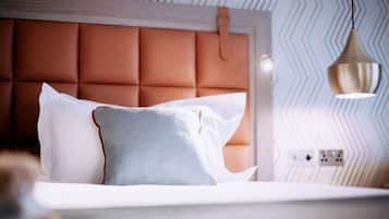 Un dormitorio con cabecera tapizada, cama con ropa de cama blanca y azul, e iluminación colgante.