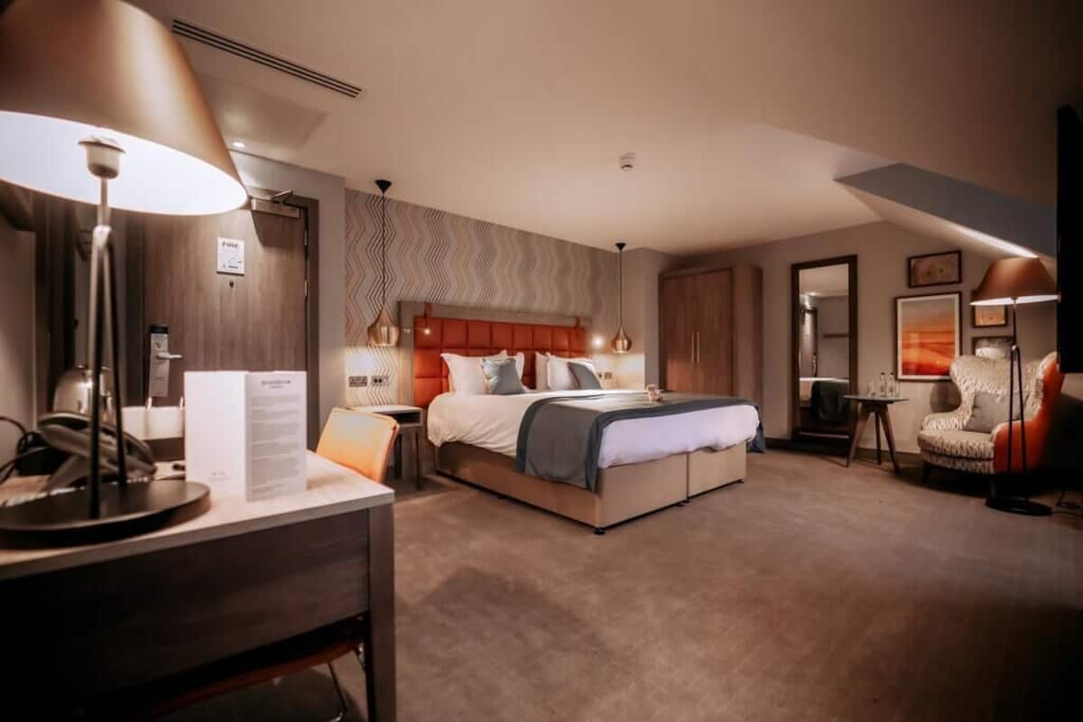 Ein Hotelzimmer mit einem großen Bett, Nachttischen, einem Schreibtisch und einem Sessel.
